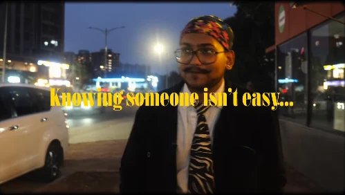 A yellow serif line, “Knowing someone isn’t easy…”, set across a night street scene, with me standing at the side in a patterned tie.